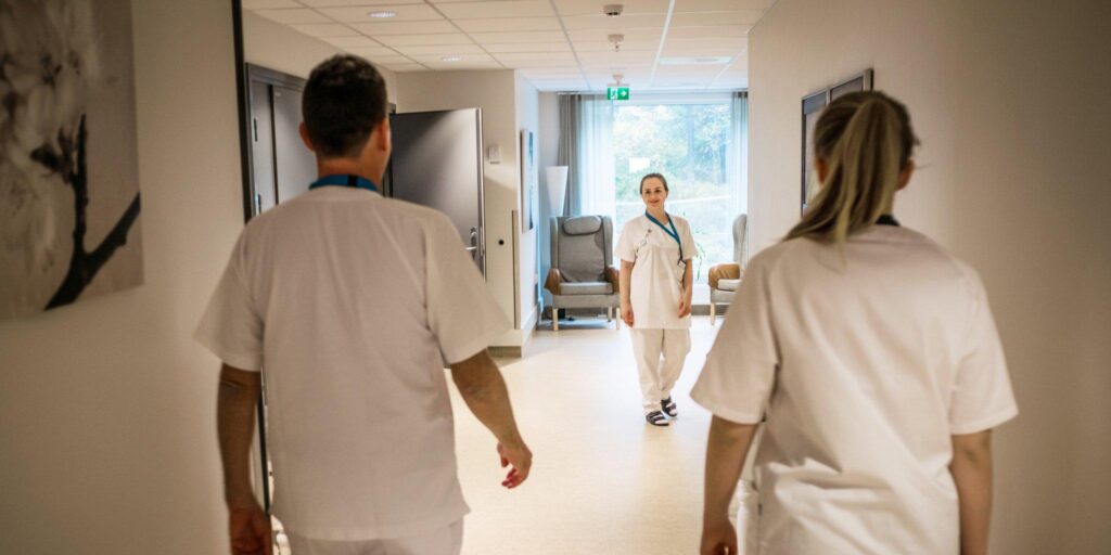 Helsefagarbeidere på jobb i sykehjem – ansatte går i korridor og møter kollega